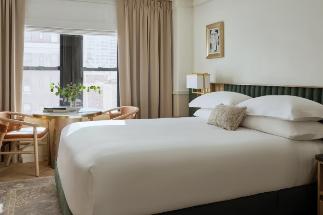 A guestroom at the hotel at 70 Park Avenue, with a large window and green upholstered headboard